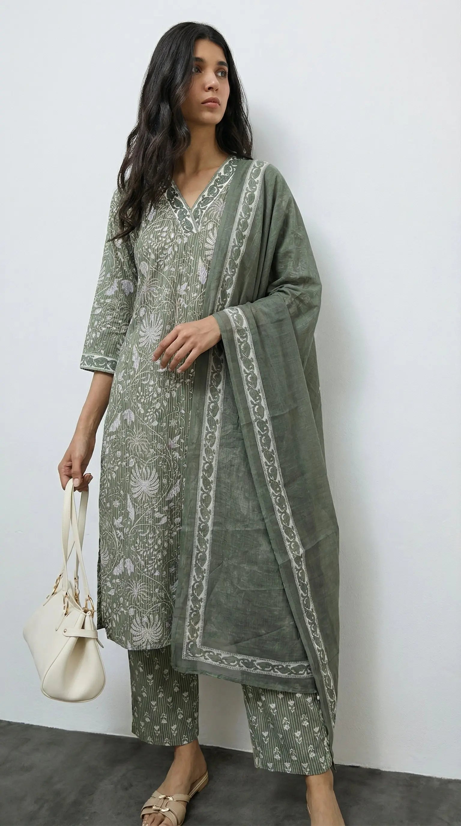 Woman wearing a green traditional outfit with a white pattern against a plain background